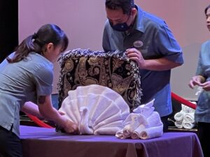 Man and woman on cruise ship demonstrating how to make a towel animal in the shape of a turkey