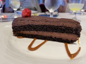 two layered chocolate mousse cake with caramel sauce swirl on plate and one raspberry on top