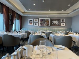 Empty dining room view at breakfast from my table for two with art on back wall and all tables set