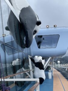 Outdoor art of large panda reaching down the wall to the small panda on the top deck of the ship