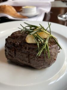 8 oz Angus Filet Mignon on a white plate with butter and green sprig on top at Chops Grille