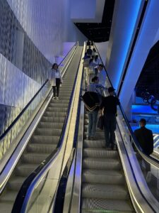 Double escalators with people ascending on the right and a lone woman descending on the left
