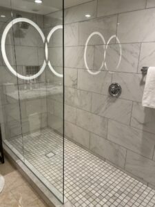 white grey marble walled walk in shower with subway tile and vanity mirror reflection