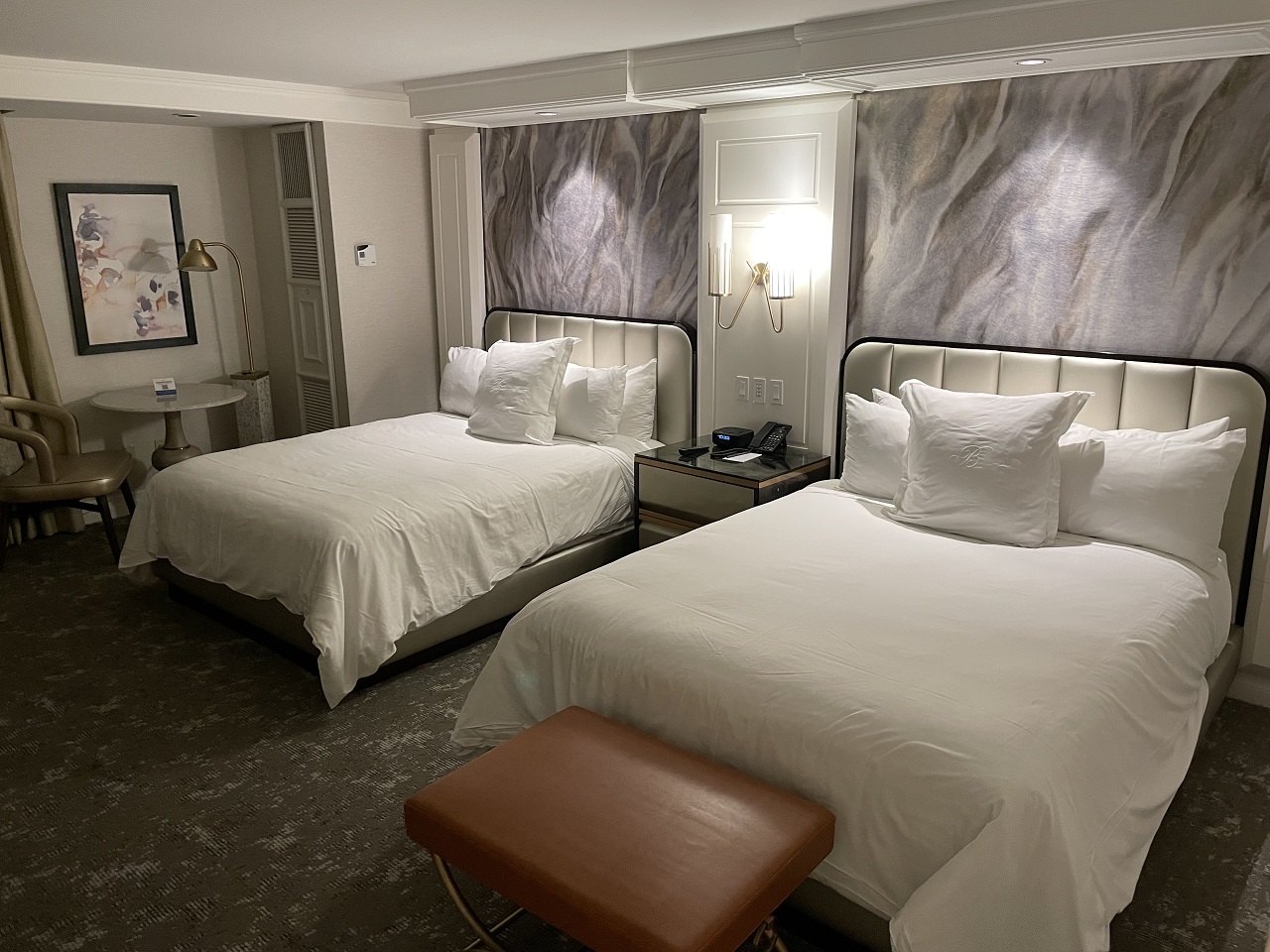 Two Queen Enhanced Hotel Room at Bellagio Las Vegas white bedding with rust colored stool and purple grey pictures