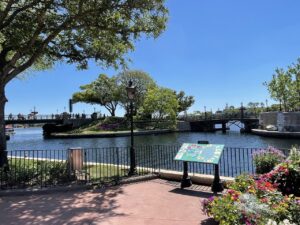 Epcot lake with black railing and trees and flowers lining on a clear blue sky day