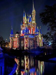 Disney World Magic Kingdom Cinderella's Castle illuminated in gold red and blue lights for fireworks show