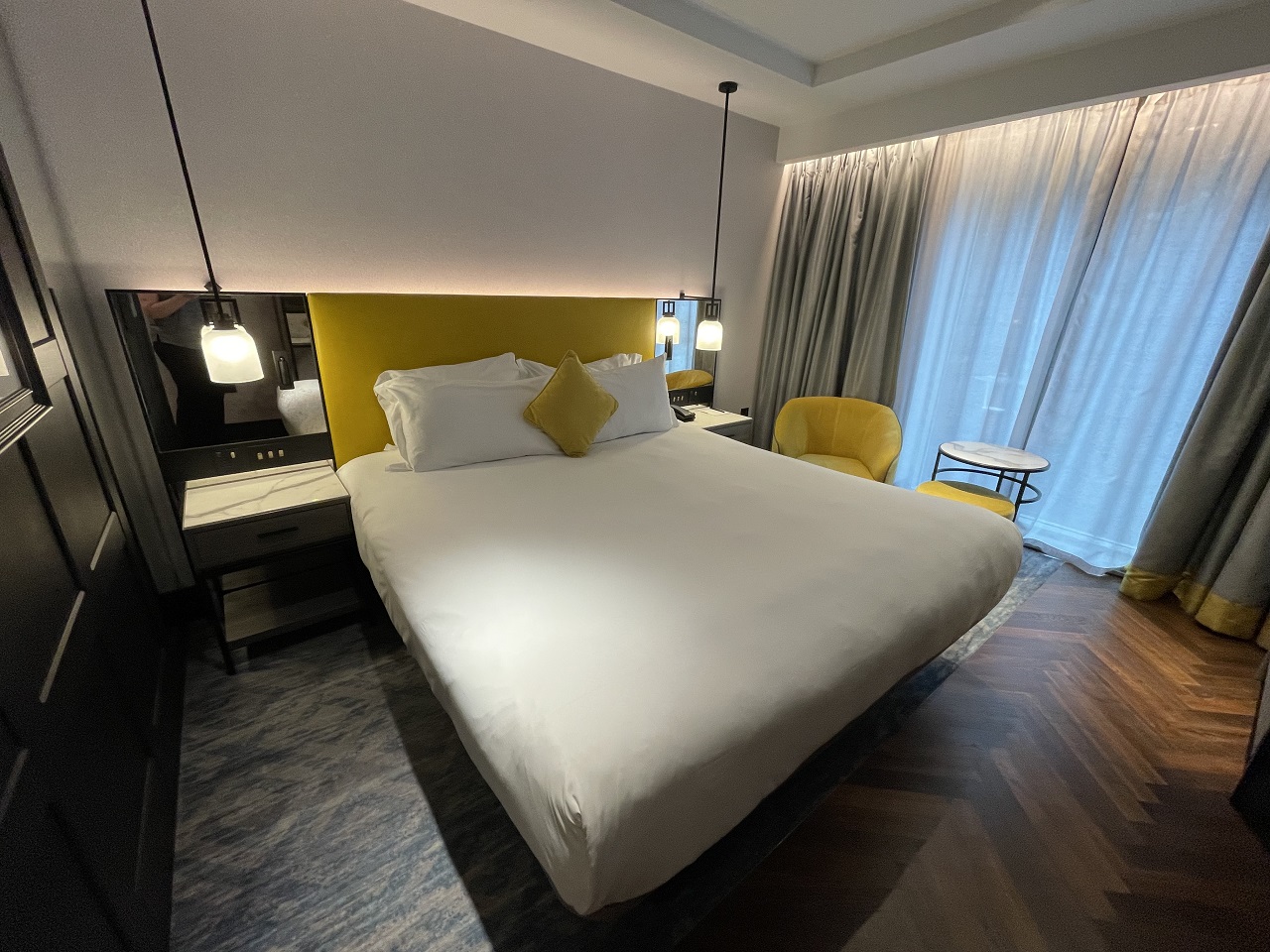 Dixon Hotel King Bed Room in London designed in white, yellow headboard and side chair with mirrors and hanging lights