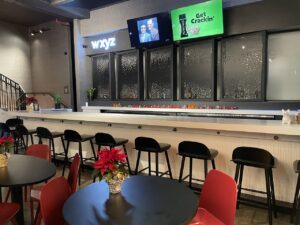 Lobby bar with empty black chairs at bar and red seats at table in foreground at Hotel Aloft Chelsea NYC