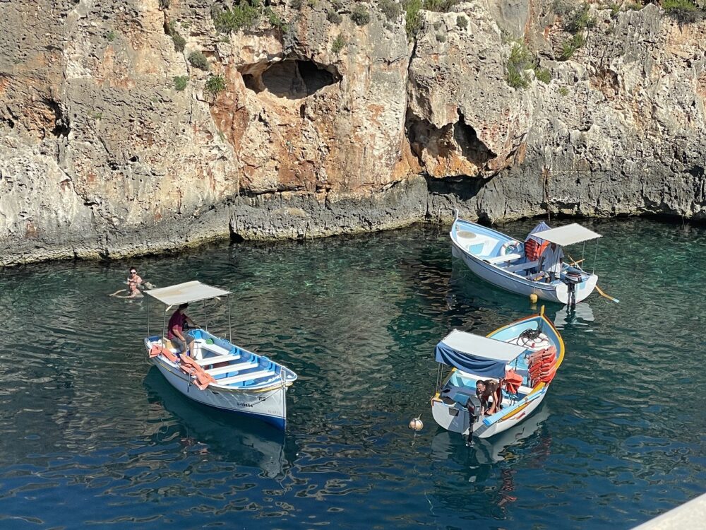 thee colorful boats in a U shape along the seaside cliffs at blue grotto